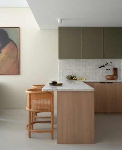 Kitchen island with marble top, wood base, cane stools, olive cabinetry, and a figurative painting on the wall