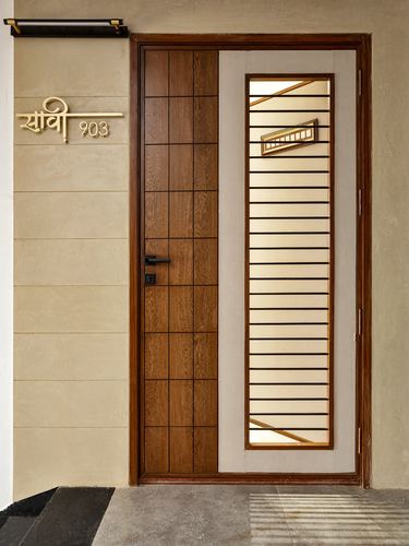Wooden entrance door with grid paneling beside a striped brass glass panel and gold nameplate