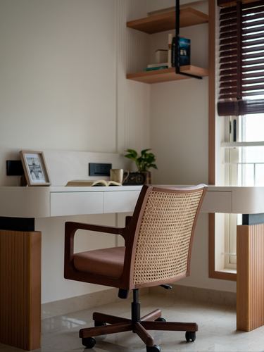 Cane-backed desk chair at white built-in desk with wooden shelf and window blinds