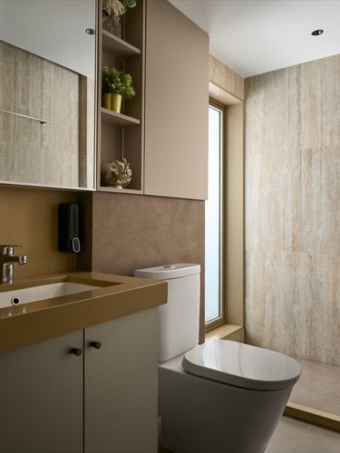 Beige stone-tiled bathroom with wall-hung toilet, brass-edged vanity and mirrored cabinet