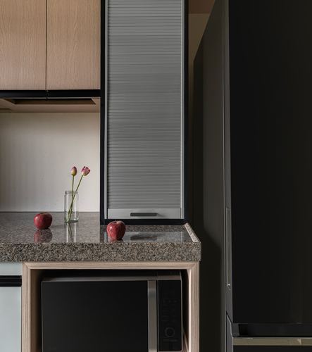 Kitchen counter with granite top, tulips, apples, and a tambour-shuttered cabinet beside a dark fridge
