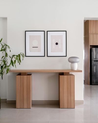 Wooden console table with block legs under two framed abstract prints and a ceramic lamp