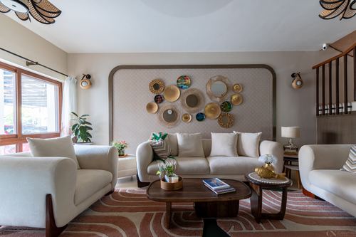 Living room with cream sofas, round wood coffee tables, and a curved wall of decorative plates and mirrors