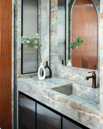 Marble vanity with carved sink, arched mirror, and orange ribbed tile reflection in Mumbai bathroom