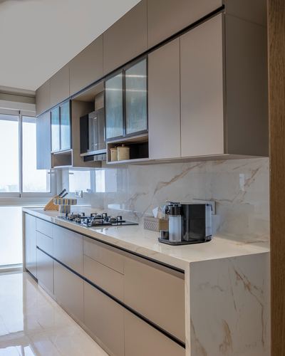 Modern galley kitchen with taupe cabinetry, veined stone backsplash and countertop, built-in cooktop.