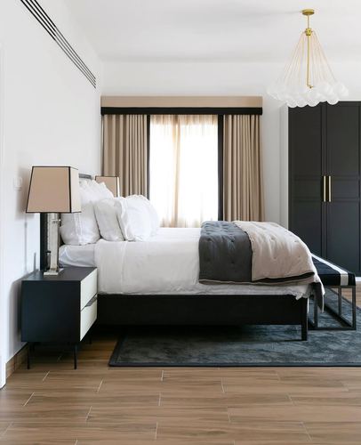 Bedroom with black upholstered bed, beige curtains, wood floor and bubble chandelier