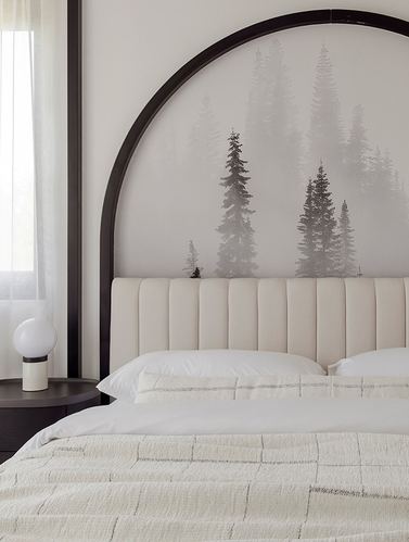 Bed with channel-tufted cream headboard beneath a black arched frame and misty forest mural, globe lamp on round nightstand