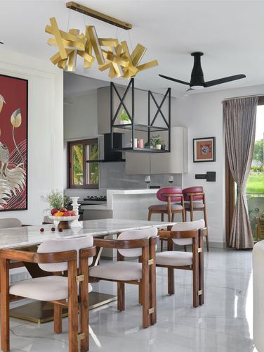 Open dining and kitchen area with marble table, wood chairs, and sculptural gold chandelier overhead