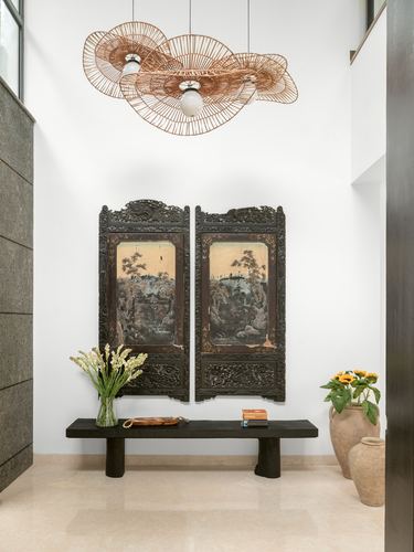 Entryway with carved wooden screen panels, woven pendant light, and black stone bench with vases