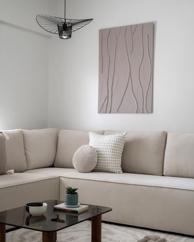 Beige sectional sofa beneath a textured wall panel and black wire pendant light in a minimalist living room