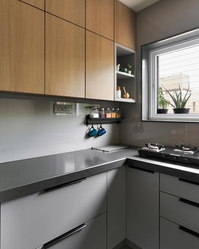 Modern L-shaped kitchen with wood-toned upper cabinets, grey countertop, and window with potted plants
