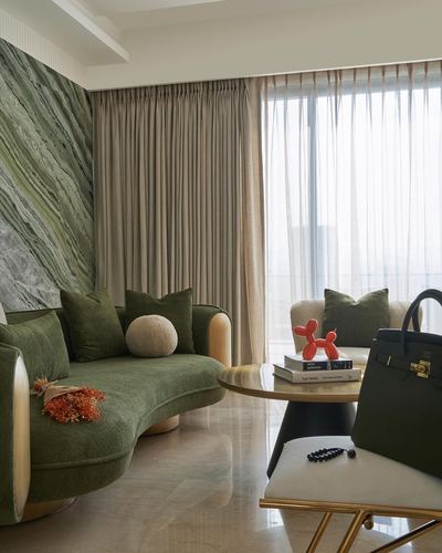 Curved olive green sofa against a green marble wall in a sunlit living room