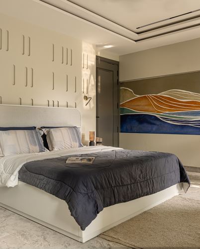 Bedroom with textured plaster wall, upholstered bed, and colorful abstract landscape artwork