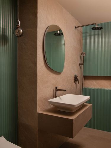 Bathroom with stone walls, oval mirror over vessel sink, fluted green tiled shower area