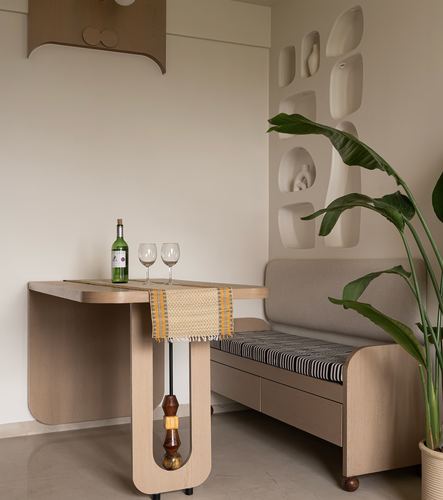 Curved wooden dining table with wine glasses beside a cushioned banquette and carved wall niches