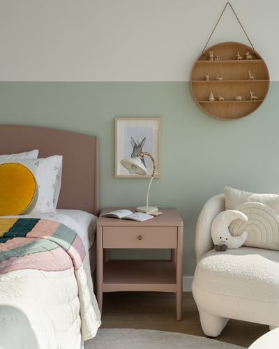Child's bedroom corner with pink bed, blush nightstand, round wooden shelf and bouclé armchair