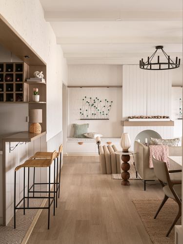 Open-plan living and dining space with wood flooring, window seat, wine rack, and round chandelier