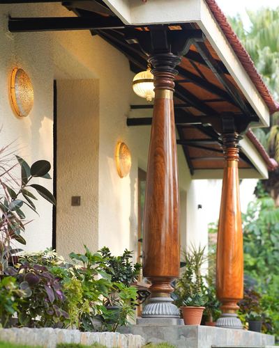 Entrance porch with turned wooden columns and sloped tiled roof surrounded by greenery