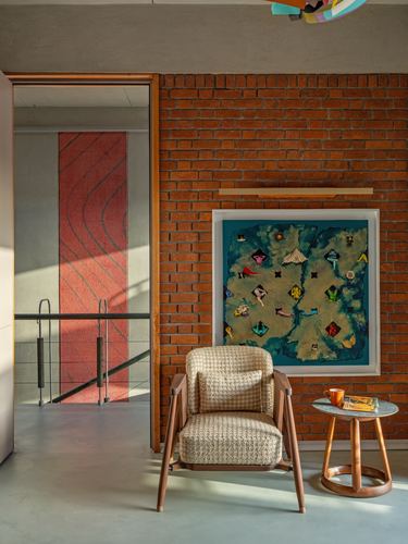 Cane and wood armchair before exposed brick wall with framed art and side table