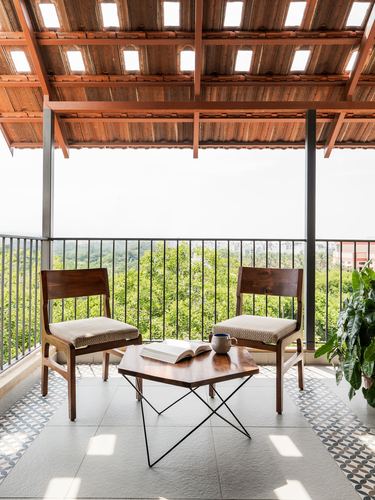 Balcony with two wooden chairs, hexagonal table, patterned tile floor, and forest view