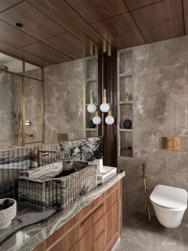 Marble-clad bathroom with ribbed stone sink, wood ceiling, brass fittings, and wall niche shelving