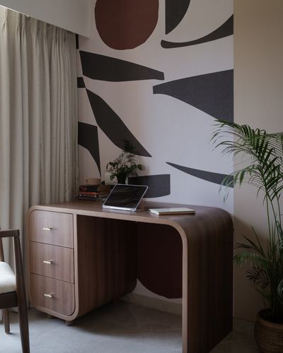 Curved walnut desk with books and tablet against a bold terracotta and charcoal mural wall