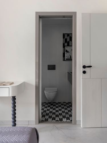View through open door into a small bathroom with chevron black-and-white floor tile and wall-hung toilet