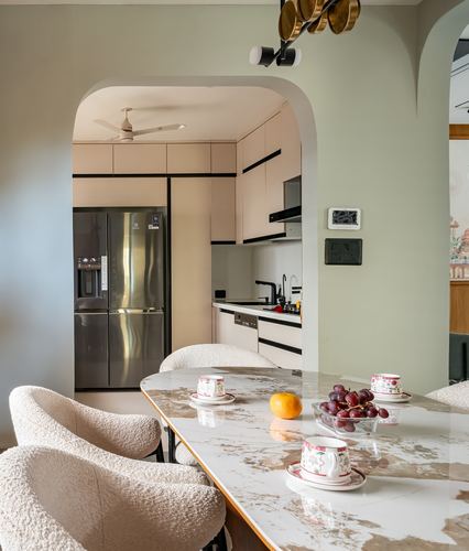 Dining table with marble-look top and boucle chairs, framed by an arch opening into a beige kitchen