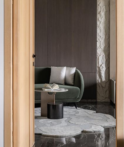 View through wooden doorway into living room with green sofa and rug on marble floor