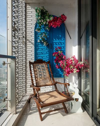 Cane planter's chair on sunlit balcony beside arched blue door with bougainvillea vines