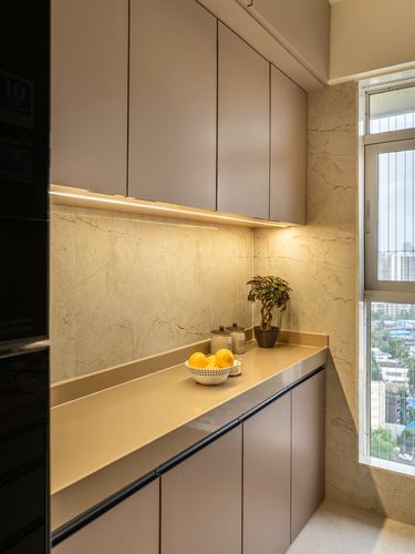 Beige kitchen counter with fruit bowl and plant under cabinet lighting, window with city view