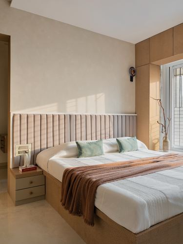 Sunlit bedroom with fluted pink headboard, wood-paneled window wall, and terracotta throw on bed