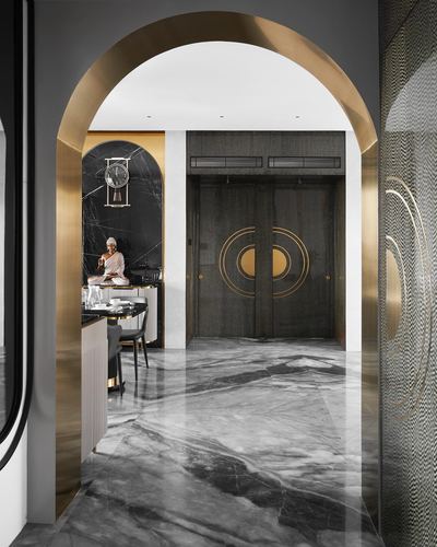 Brass archway frames a marble corridor leading to dark double doors with gold medallion