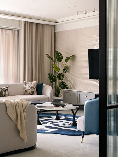 Beige living room with curved sofa, marble coffee table, navy rug and textured wall panel