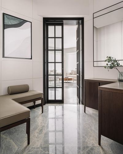 Marble-floored foyer with black-framed glass door opening to living room, taupe bench and wood sideboard