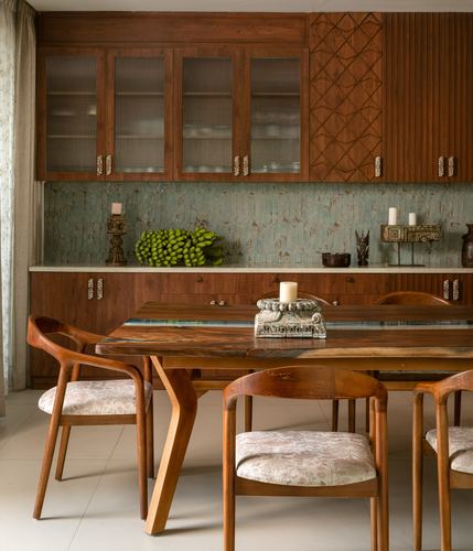 Dining area with wooden table, curved chairs, and carved wood cabinetry over a textured green backsplash