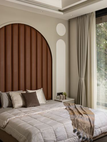 Bedroom with arched rust-colored tufted headboard, beige linens, and floor-to-ceiling curtains beside a window