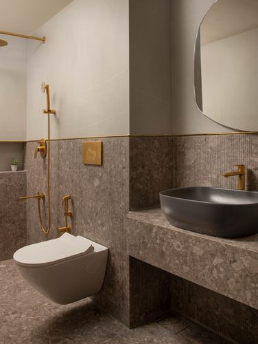 Bathroom with fluted stone walls, brass fixtures, wall-hung toilet and dark vessel sink