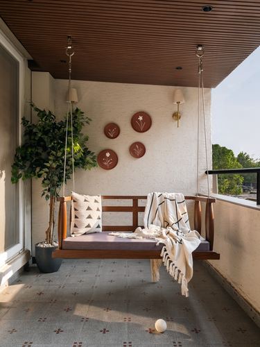 Wooden hanging swing on a balcony with terracotta wall plates and a potted plant