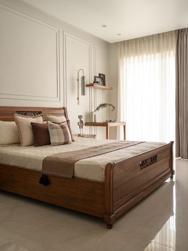 Bedroom with carved wooden bed, panelled wall, brass sconce, and sheer curtained window