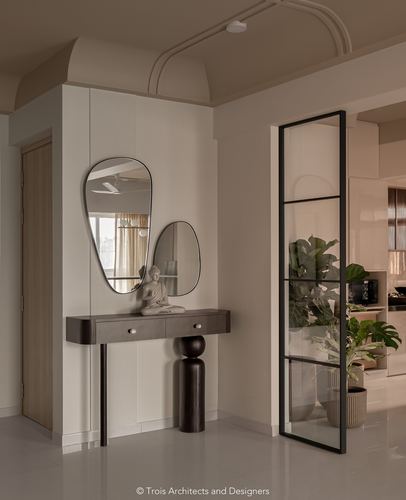 Beige foyer with two irregular mirrors over a dark curved console and black-framed glass door