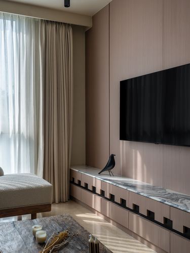 Beige-toned living room with sheer curtains, marble console under a wall-mounted tv, and a black bird sculpture.
