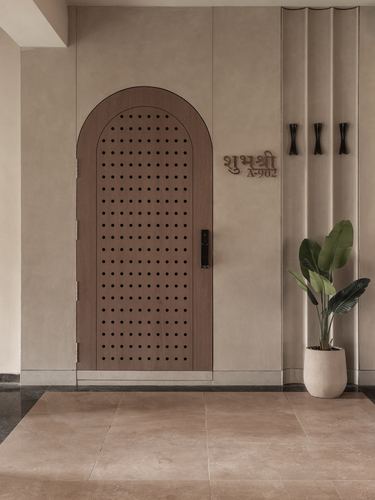 Arched perforated wooden door beside fluted wall with plant and nameplate in foyer