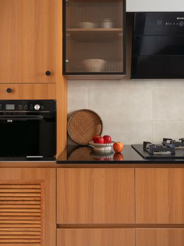 Warm wood kitchen cabinetry with black chimney hood, glass-fronted cabinet, and fruit on dark countertop