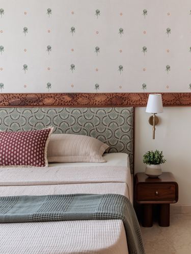 Bedroom corner with carved wood border, sage patterned headboard, wall sconce and wood nightstand