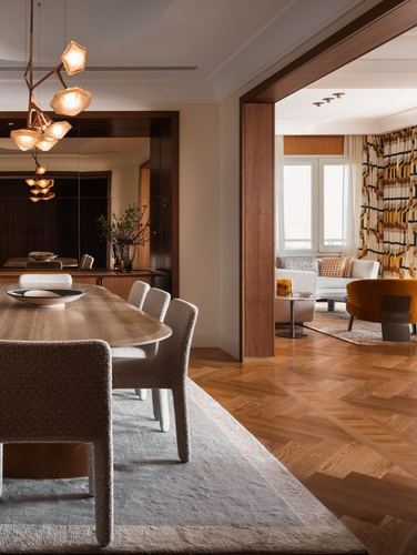 Dining room with sculptural pendant, mirrored wall, opening to living room with patterned curtains