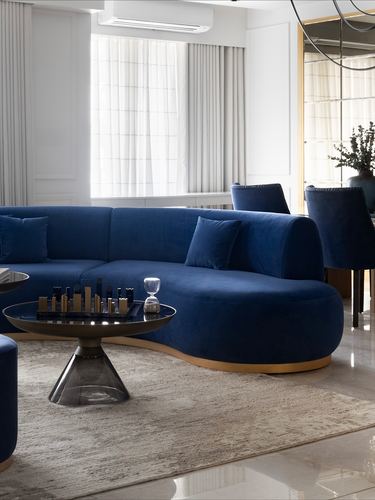 Curved navy blue velvet sofa with round brass-based coffee table in a neutral living room