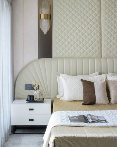 Beige quilted headboard with brass wall sconce, white nightstand, and styled bed with cushions and magazine