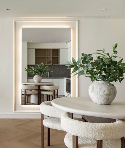 Neutral dining nook with round stone table, boucle chairs, and a large backlit mirror reflecting the kitchen