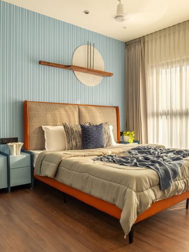 Bedroom with orange leather-trimmed bed, woven headboard, fluted blue wall and wooden sconce